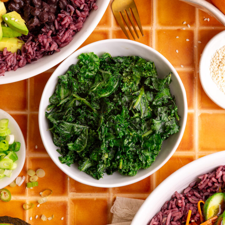 A bowl of bibibop style honey citrus kale, with two bibibop-style bowls.