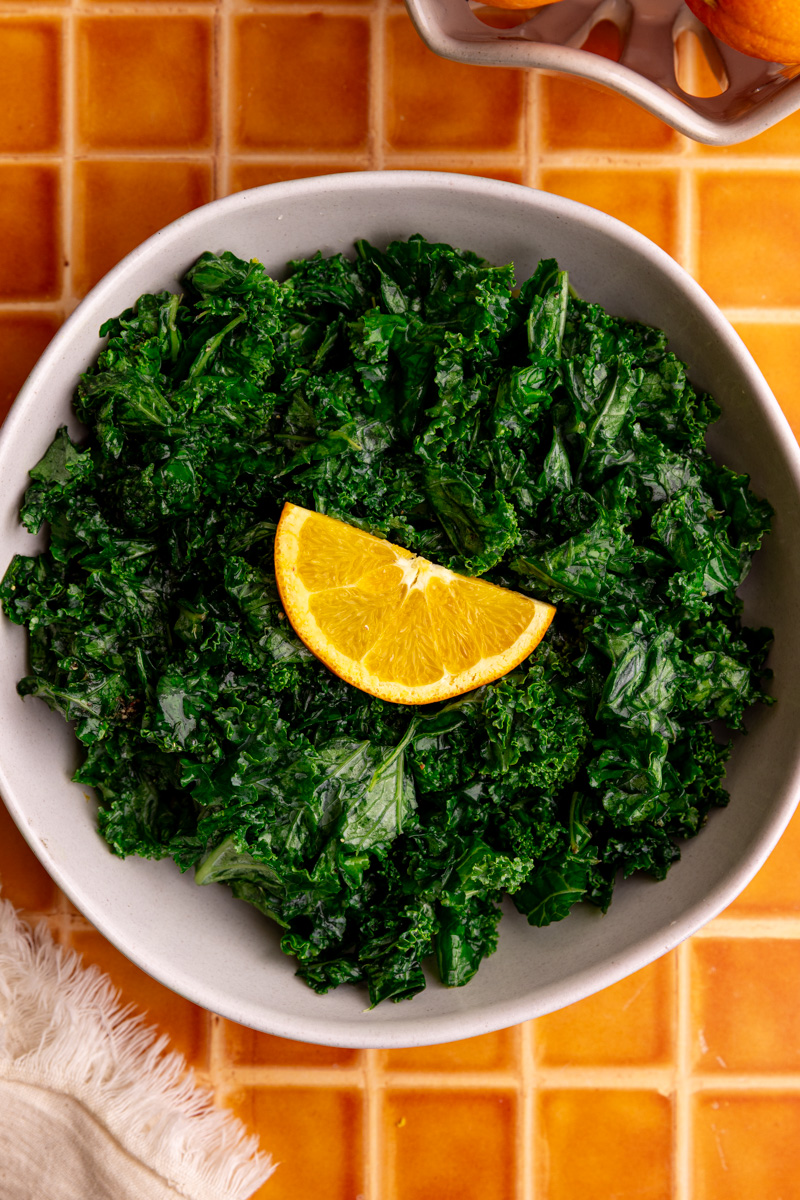 A bowl of honey citrus kale, garnished with an orange slice.