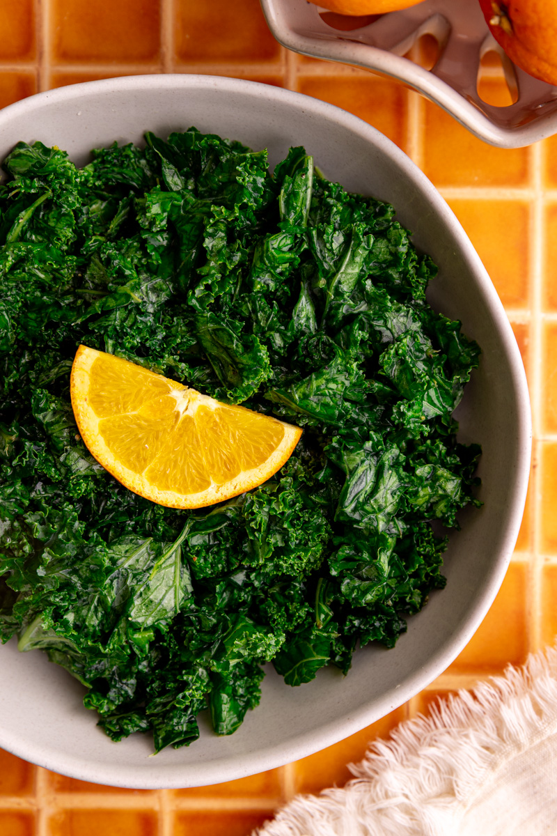 A bowl of honey citrus kale, garnished with an orange slice.