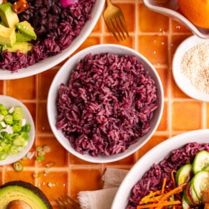 A bowl of homemade purple rice, next to two bibibop-style bowls.