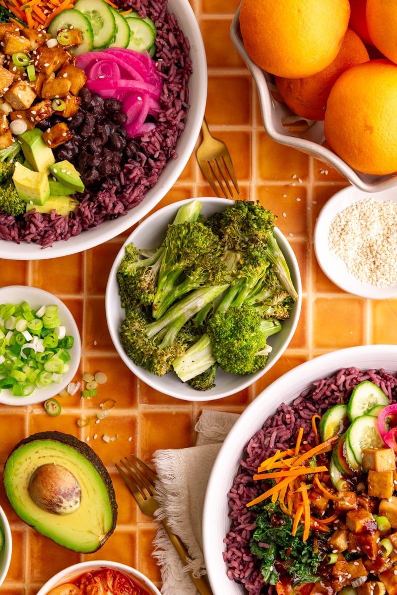 A bowl of homemade sesame broccoli, next to two bibibop-style bowls.