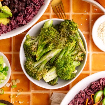A bowl of homemade sesame broccoli, next to two bibibop-style bowls.
