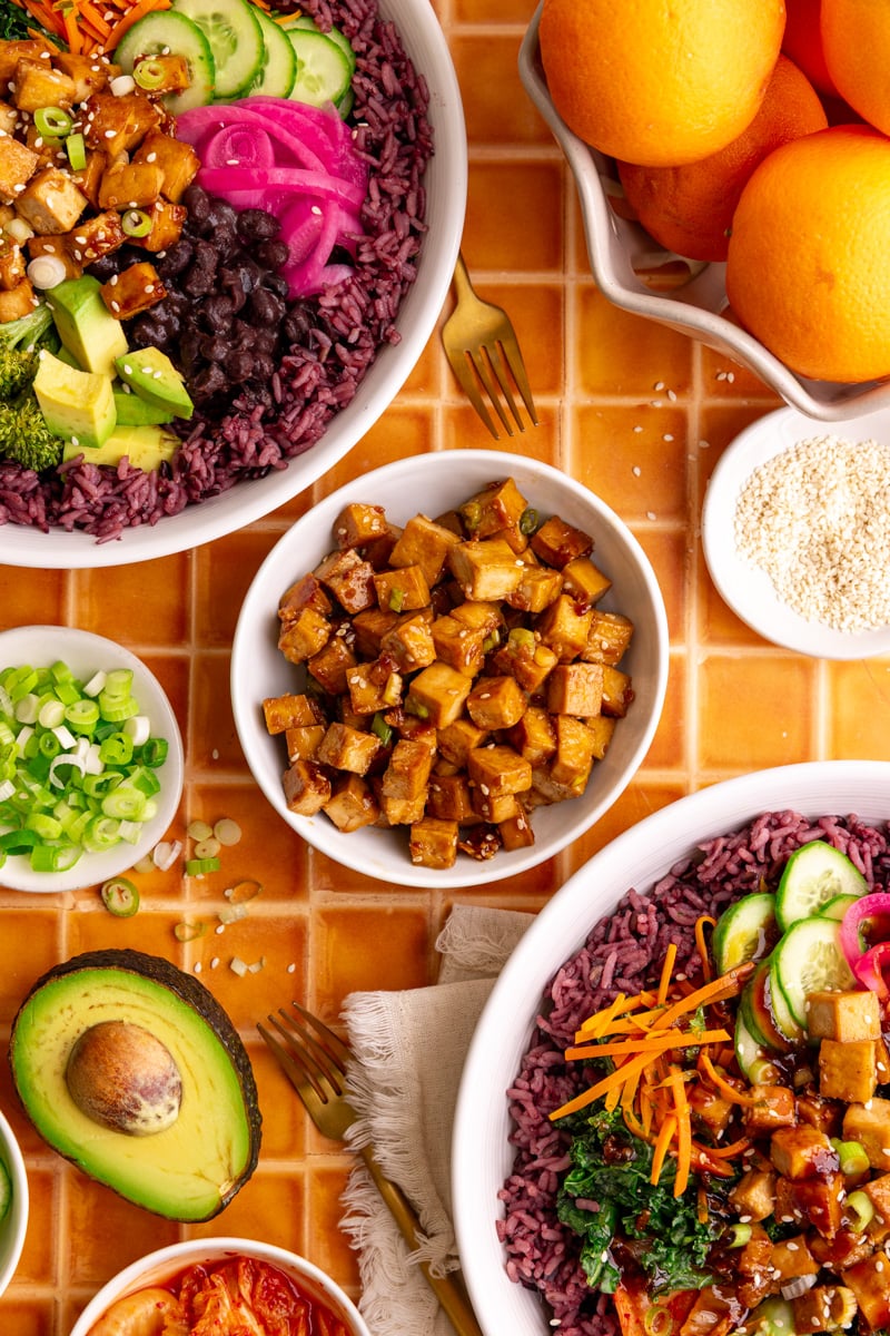 A bowl of freshly cooked tofu, next to two bibibop-style bowls.
