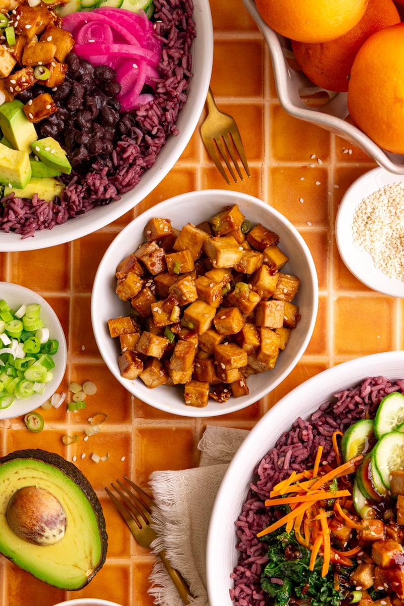 A bowl of freshly cooked tofu, next to two bibibop-style bowls.