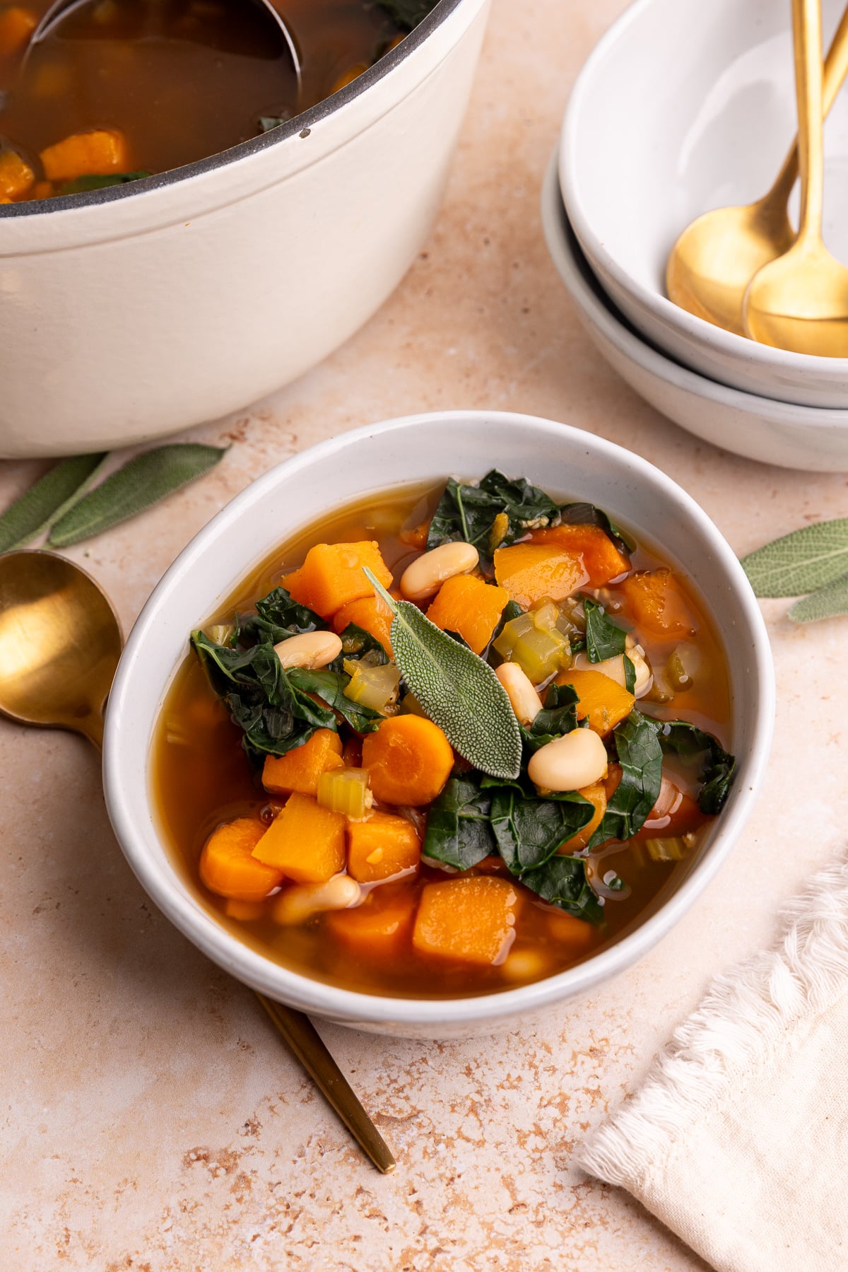A bowl of vegan harvest vegetable soup, garnished with a fresh sage leaf.