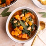A bowl of vegan harvest vegetable soup, garnished with a fresh sage leaf.