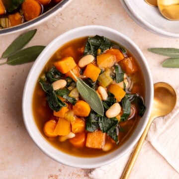 A bowl of vegan harvest vegetable soup, garnished with a fresh sage leaf.