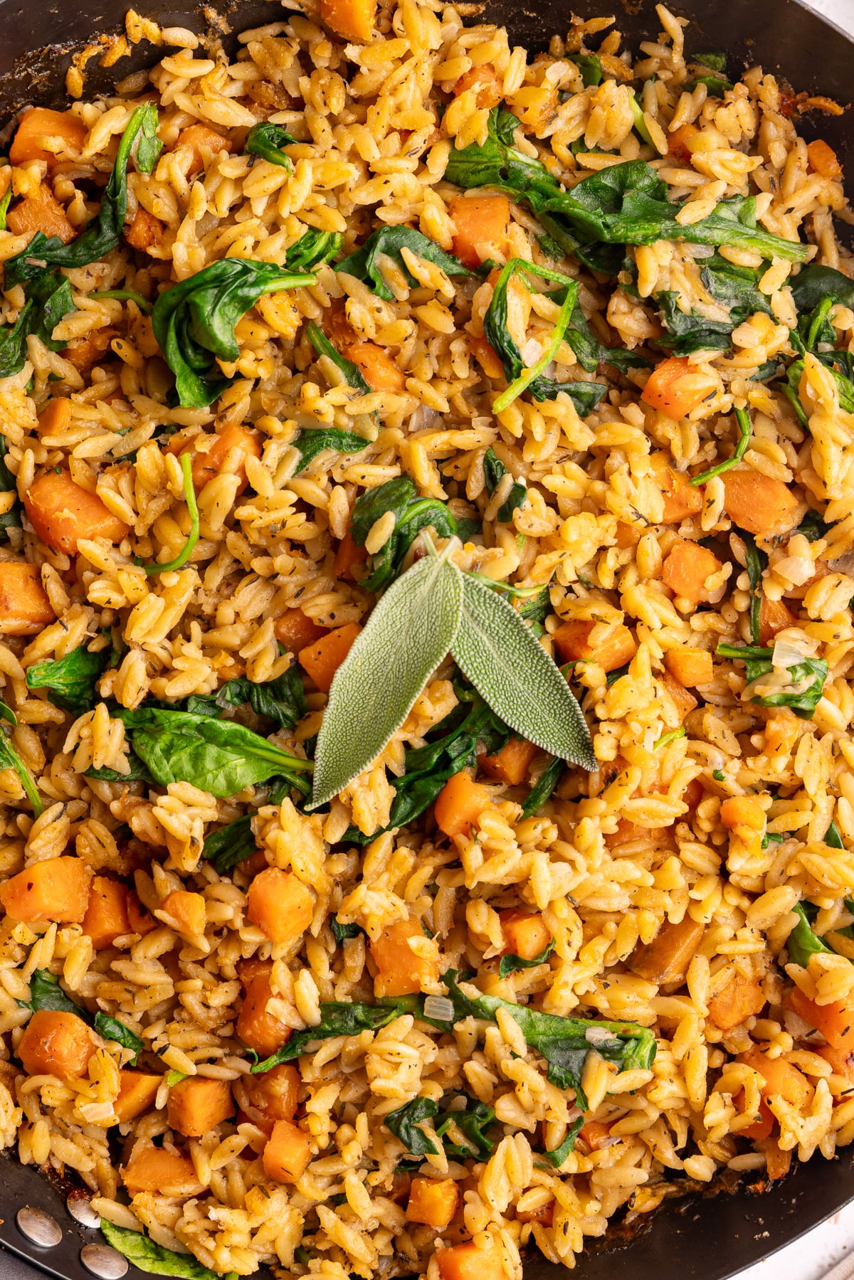 A pan of freshly baked vegan sweet potato baked orzo, garnished with two sage leaves.