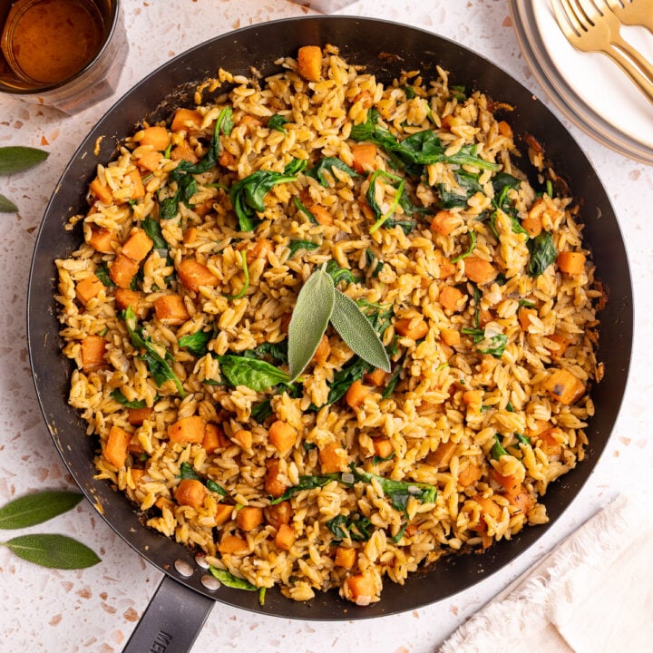 A pan of freshly baked vegan sweet potato baked orzo, garnished with two sage leaves.
