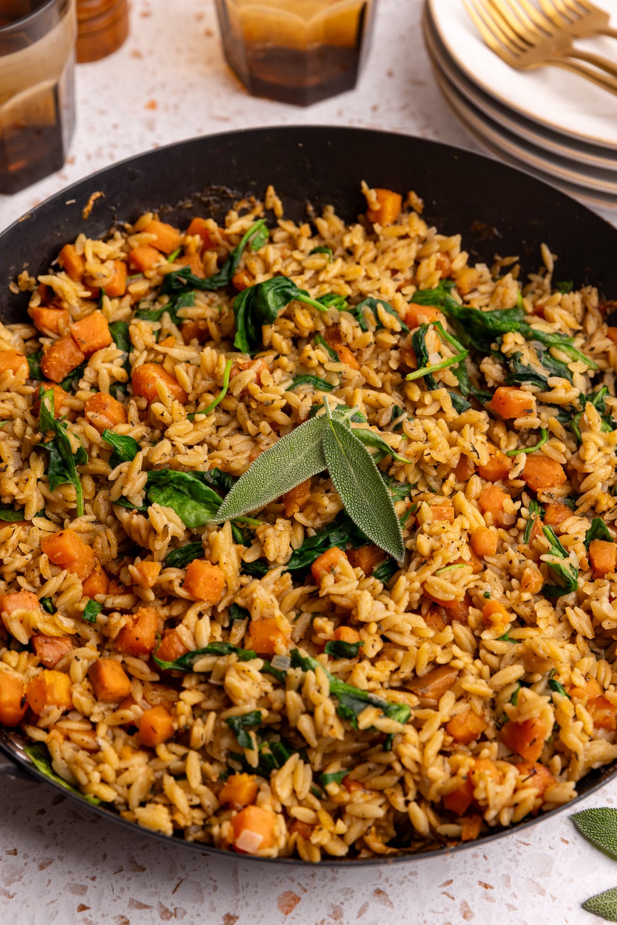 A pan of freshly baked vegan sweet potato baked orzo, garnished with two sage leaves.
