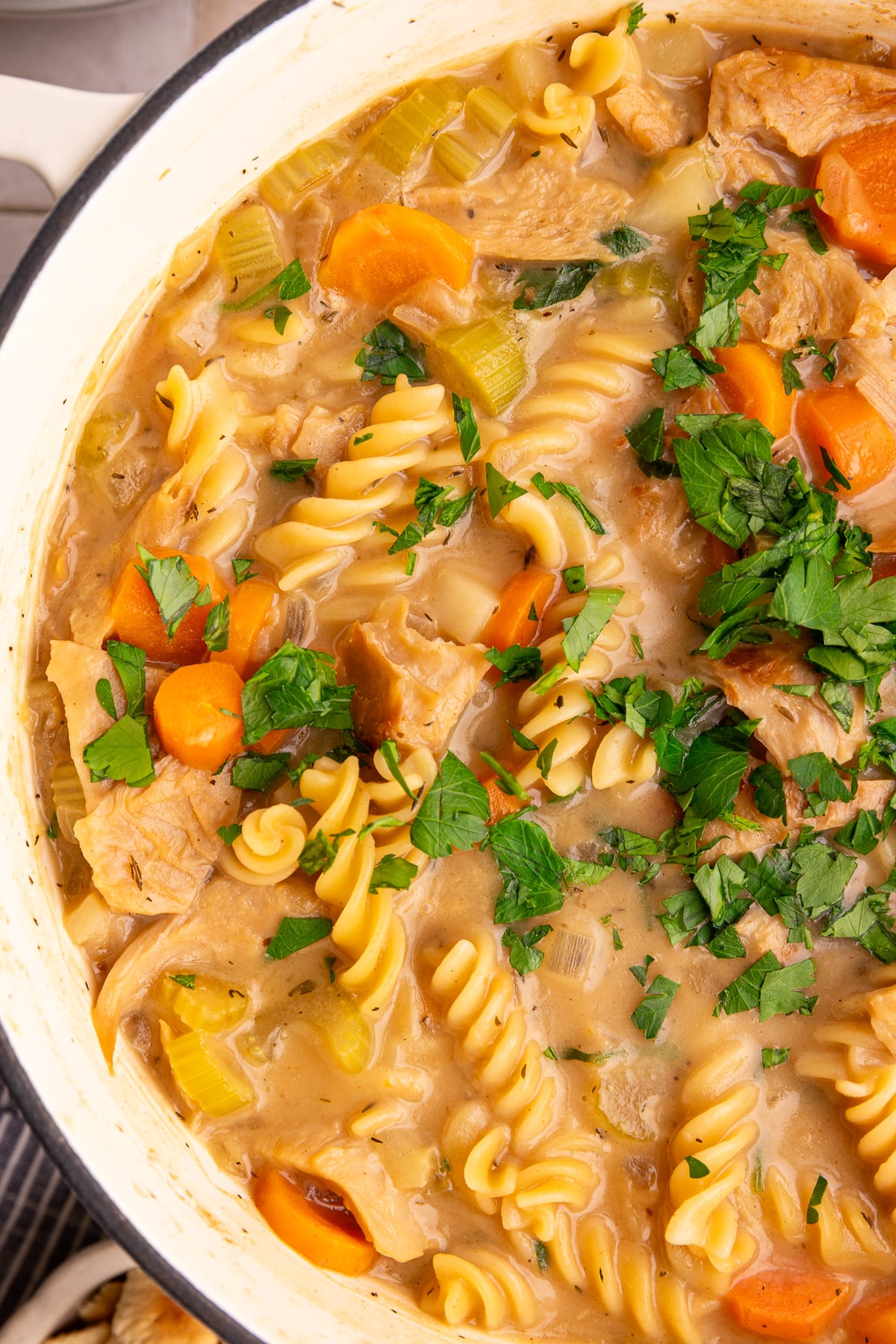 A pot of freshly cooked vegan creamy chicken noodle soup, with a sprinkle of fresh parsley.