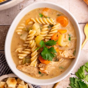 A bowl of vegan creamy chicken noodle soup, garnished with parsley.